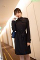 A woman in a black trench coat is posing for a picture.