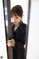 A woman in a black trench coat looking at herself in the mirror.