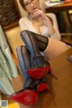 A woman sitting at a table with a pair of red high heels.