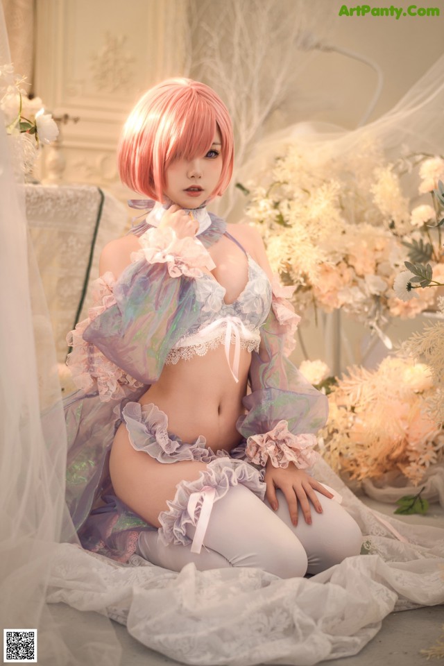 A woman with pink hair sitting on a bed.