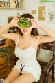 A woman sitting on a chair holding a watermelon over her eyes.