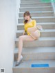 A woman in a yellow top and white pantyhose sitting on some stairs.