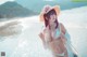 A woman in a bikini and hat standing on a beach.