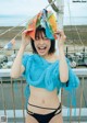 A woman in a blue top and black bikini holding a colorful hat.