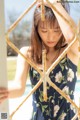 A woman in a blue floral dress leaning against a fence.