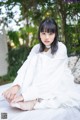 A woman in a white dress sitting on a bed.