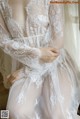 A woman wearing a white lace robe sitting on a window sill.