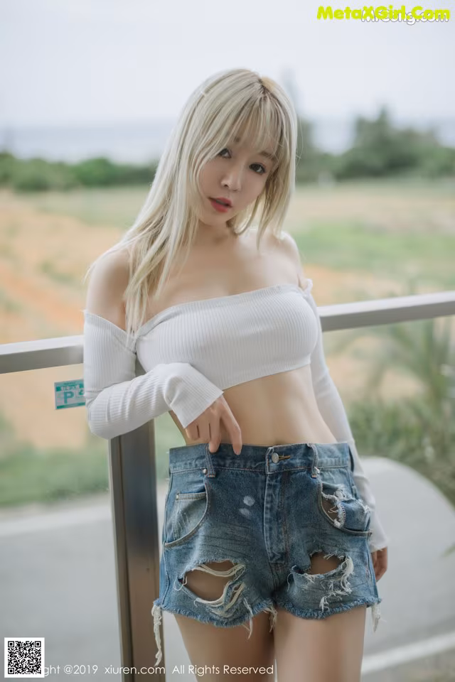 A woman in a white top and denim shorts posing for a picture.