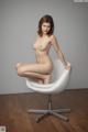 A nude woman sitting on a white chair.