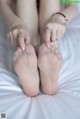 A woman is putting on her bare feet on a bed.