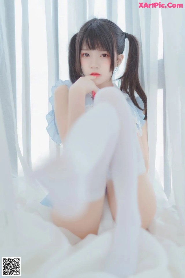A young woman sitting on a bed in a white dress.
