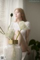 A woman sitting on a window sill next to a vase of flowers.