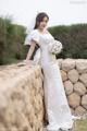 A woman in a wedding dress leaning against a stone wall.