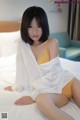 A woman in a white shirt and yellow panties sitting on a bed.