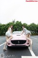 A couple of women standing next to a pink car.