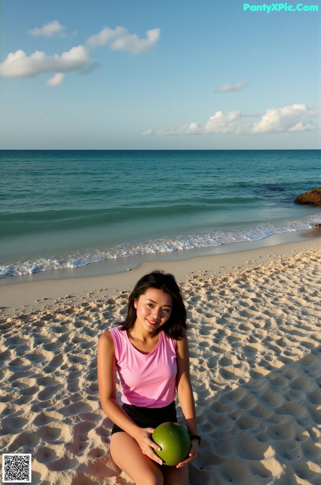 A woman sitting on a beach holding a green ball.