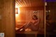 A naked woman sitting on a bench in a sauna.