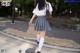 A woman in a white shirt and gray skirt is walking down the street.