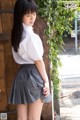 A woman in a white shirt and gray skirt leaning against a wooden door.