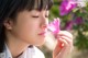 A woman smelling a pink flower in front of a bush.