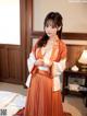 A woman in an orange and white kimono holding a cup of tea.