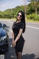 A woman in a black dress and sunglasses standing next to a car.