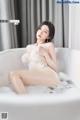 A naked woman sitting in a bathtub filled with foam.