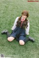 A woman in a school uniform sitting on the grass.