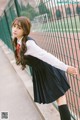 A woman in a school uniform leaning against a fence.