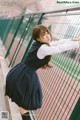 A woman in a school uniform leaning against a fence.