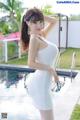 A woman in a white dress posing by a pool.