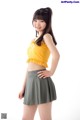 A woman in a yellow top and gray skirt posing for a picture.