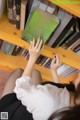 A woman sitting on the floor in front of a bookshelf holding a book.