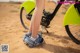 A person standing next to a green bike on a dirt road.